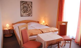 A cozy bedroom with a double bed and soft color tones. A small table with two chairs and a window with curtains create an inviting atmosphere.