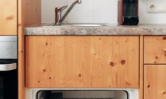A modern kitchen corner with a dishwasher and a coffee machine. Wooden cabinets and a stone countertop complement the overall picture.