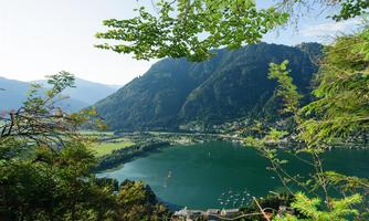 A picturesque landscape with a clear lake, surrounded by green mountains. The scene is complemented by blooming trees in the foreground.