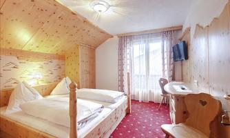 A cozy bedroom with wooden interior and two beds. The room has a window looking outside and a small table with a chair.