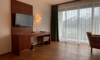 A cozy living space with a television and a desk. Large windows let in plenty of daylight and offer a view of the mountains.