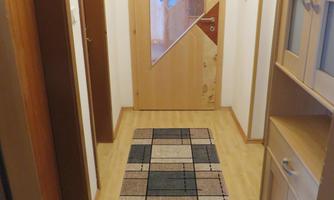 A narrow hallway with a patterned carpet on the floor. The walls are light, and there is a large wooden door with a glass window.