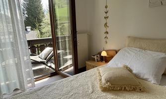 A cozy bedroom with a large window and a view of the terrace. The room is bright and friendly, with a comfortable bed and decorative elements.