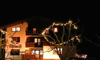 A cozy house with warmly lit windows at night. Trees with lights surround the building.