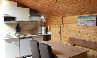 A cozy kitchenette in a wooden house with a dining table and chairs. The kitchen is modern and well-equipped.