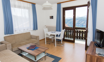 A cozy living room with a sofa, a table, and a television. Large windows offer a view of the mountains and let in plenty of light.