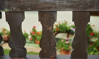 A wooden railing with decorative elements. In the background, blooming plants are visible.
