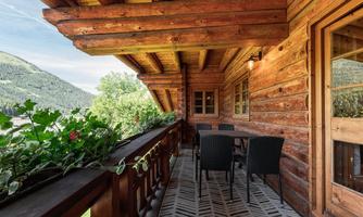 A beautiful wooden balcony with a view of the mountains. There is a table and chairs, as well as some plants.
