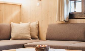 A cozy living room with a gray sofa and a wooden table. On the table, there is a small basket with apples.