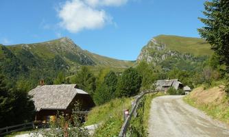 A tranquil mountain landscape with rugged hills and green forests. Along the way, there are some traditional wooden houses visible.