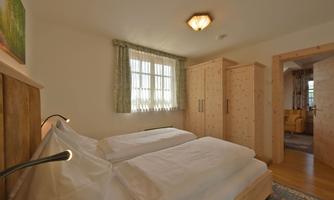 A cozy bedroom with two separate beds and wooden-clad furniture. A large window provides plenty of light and an inviting space.