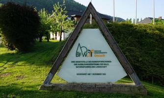 A sign of the BFW in Germany displays information about a training facility for nature and landscape. The surroundings are green and surrounded by trees.