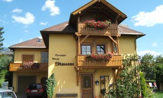 A beautiful yellow house with an expanded balcony and blooming flower boxes. The surroundings are green and inviting, ideal for a stay.