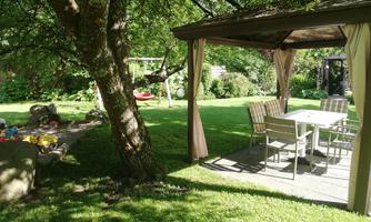 An inviting garden with a gazebo and a table with chairs. The green lawn is surrounded by trees, creating a tranquil atmosphere.
