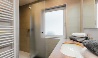 A modern bathroom with a glass shower and a large window. Several towels in different colors are laid out on the sink.