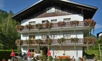 A charming building with several balconies adorned with flowers. In front of the house are umbrellas and a cozy seating area.