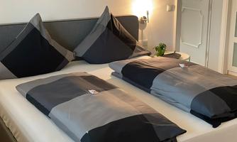 A cozy bedroom with a double bed and modern, multicolored bedcovers. The pillows are also stylish, and the wall has a simple design.
