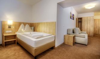 A modern hotel room with a double bed, a table, and cozy armchairs. Bright walls and wooden paneling create an inviting atmosphere.
