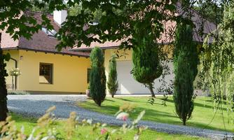 A beautiful house with a yellow paint job and a red-covered roof. Surrounded by well-kept lawn and tall cypress trees.