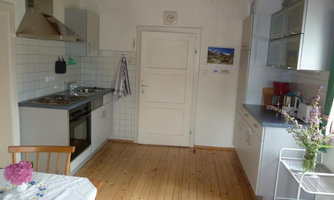 A bright kitchen with wooden flooring and modern appliances. A vase with flowers is on the table.