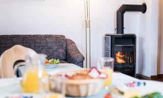 A cozy living room with a sofa and a wood stove. Drinks and fresh fruit are on the table.