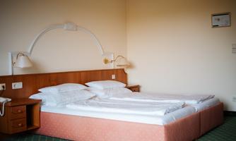 A simple hotel room with two beds and white bed linen. The walls are neutrally colored and there are night lamps on both sides.