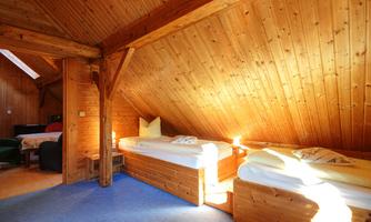 A cozy wooden room with two beds and a warm, inviting ambiance. The roof is slanted and made of wood, creating a rustic atmosphere.