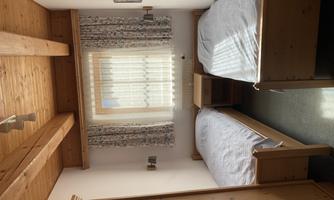 A simple bedroom with two single beds. There is a window with curtains and wooden ceilings.