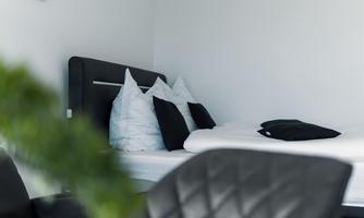 A modern bedroom with a bed and several pillows. In the foreground, stylish black chairs are visible.