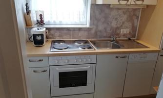 A modern kitchen with a stove, a sink, and a dishwasher. The room is bright and has a friendly atmosphere.