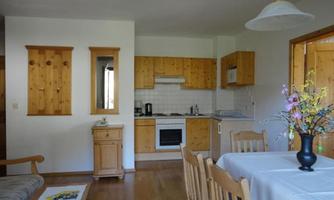 A cozy kitchen with wooden shelves and a dining table for several people. Next to the table is a sofa, making the space inviting.