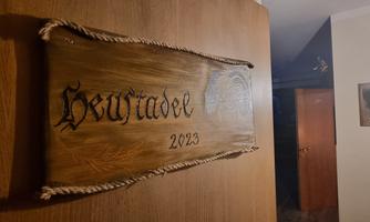 A wooden wall sign with the inscription "Heuwiadel 2023". It is attached to a door and has a rustic appearance.