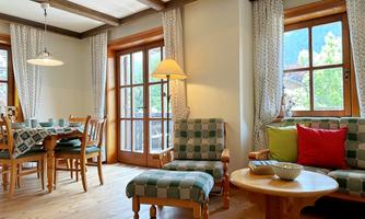 A cozy living space with a dining area and large windows. The furniture is made of wood, and the decoration is in warm colors.