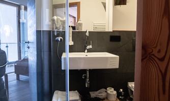 A modern bathroom with a glass shower and an elegant sink. The walls are tiled black and the decor is minimalist.