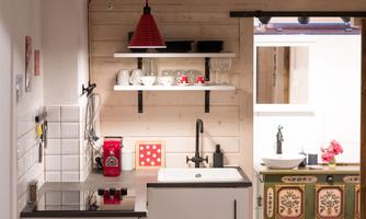 A modern kitchen with a white sink and a cooking surface. In the background, you can see a dining table and a colorful dresser.