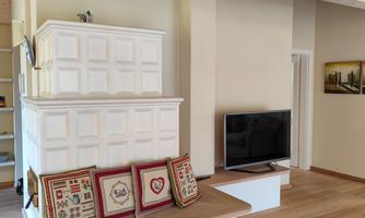 A modern living room with wooden flooring and large windows. On a cozy bench lie decorative cushions.