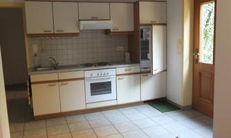 A bright kitchen with white cabinets and a gas stove. The door leads outside, and the floor is tiled.