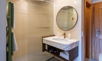 A modern bathroom with a round mirror and an elegant sink. The walls are painted in soft colors and there are towels on a shelf.
