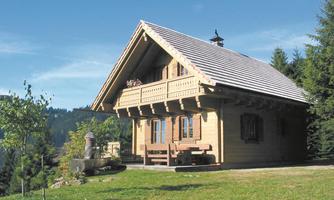 A charming wooden house with a traditional roof amidst trees. The green meadow and the clear sky create a picturesque surroundings.