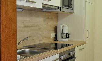 A modern kitchen with white cabinets and wooden details. It is well-equipped with a stove, oven, and microwave.