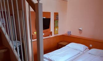 A cozy room with two single beds, wooden floor, and stairs. The space is bright and cheerfully designed.