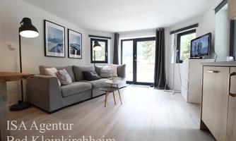 A modern living room with a cozy couch and large windows that let in plenty of daylight. The space is bright and minimally furnished.