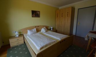 A simple bedroom with two single beds and light wood furniture. The walls are painted yellow and a carpet lies on the floor.