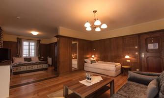 A cozy room with wood paneling that features a seating area and a double bed. Large windows let in plenty of daylight.