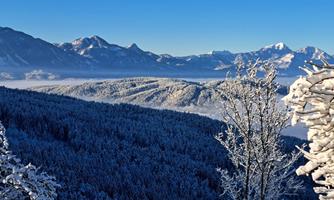 An impressive winter landscape with snow-covered mountains and forests. The sky is clear and blue, making the view even more beautiful.