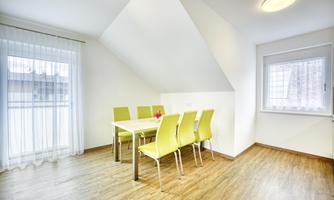 A bright room with a table and six green chairs. Large windows provide plenty of daylight.
