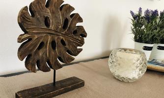 A decorative wooden sculpture in the shape of a leaf is standing on a table. Next to the sculpture is a glass lantern and a small plant.