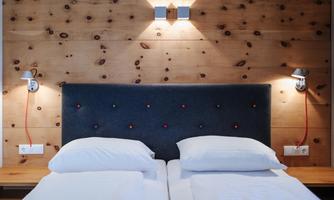 A modern bedroom with a wooden wall and a padded headboard. The room is well-lit and features two separate beds.