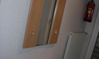 A wooden wardrobe with a mirrored door and space for jackets. Next to it, there is a small shelf with drawers.