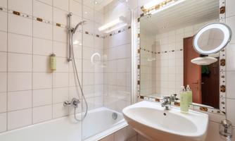 A modern bathroom with a bathtub and a shower. A sink with a mirror and personal care products is also visible.